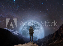 Fototapeta pltno 330 x 244, 205708981 - a man with backpack standing on mountain peak at night, and silhouette mountain with bright full moon and sky full of stars