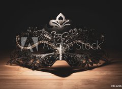 Fototapeta vliesov 100 x 73, 311256147 - A portrait of a traditional venetian mask on a wooden surface appearing mysteriously out of the darkness.