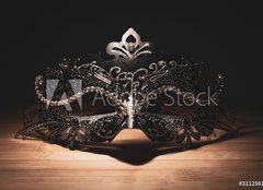 Fototapeta pltno 160 x 116, 311256147 - A portrait of a traditional venetian mask on a wooden surface appearing mysteriously out of the darkness.