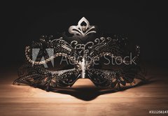 Fototapeta pltno 174 x 120, 311256147 - A portrait of a traditional venetian mask on a wooden surface appearing mysteriously out of the darkness.