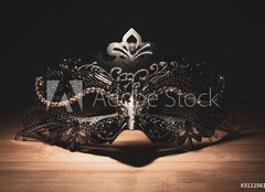 Fototapeta papr 254 x 184, 311256147 - A portrait of a traditional venetian mask on a wooden surface appearing mysteriously out of the darkness.