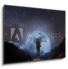 Obraz 1D - 100 x 70 cm F_E205708981 - a man with backpack standing on mountain peak at night, and silhouette mountain with bright full moon and sky full of stars